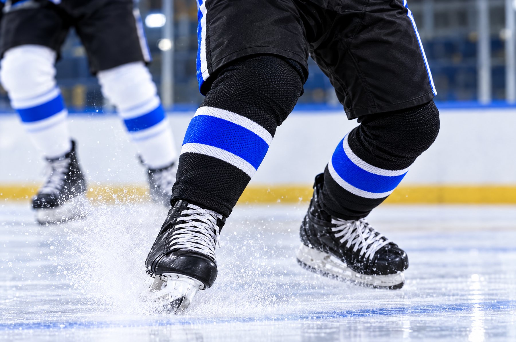 Bas de hockey noirs à rayures bleu électrique et blanches lors d'un freinage brusque, avec gerbe de glace